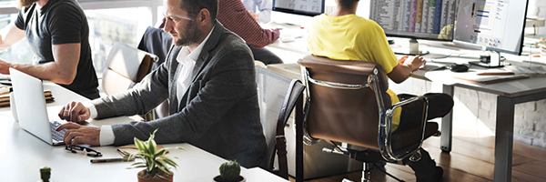 Employés de bureau assis à leur bureau et utilisant divers types d'appareils et de terminaux.